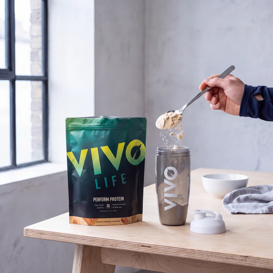 Krok 2: wsypywanie odmierzonej porcji PERFORM słony karmel łyżką stołową do shakera Vivo Life, obok opakowanie 936 g